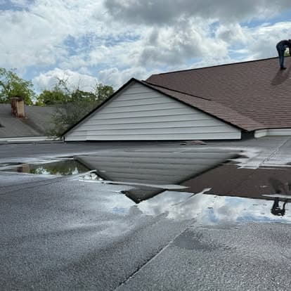 Roofer inspecting a residential roof with water reflections on the surface under cloudy skies.