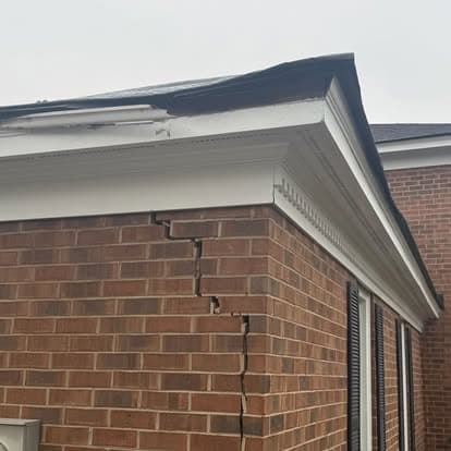 Cracked brick wall due to structural damage around roofline on a residential building.