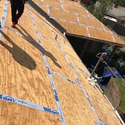 Person walking on a plywood roof deck secured with roof tape, preparation for roofing installation.