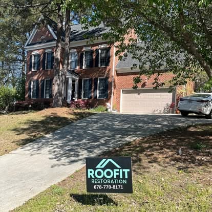 Brick house with black shutters and a RoofFit Restoration sign in front yard.