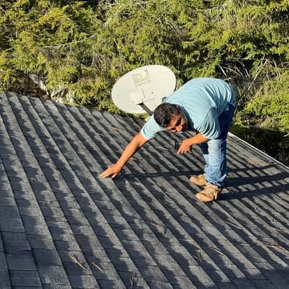 Roof inspector assessing roofing materials on a residential home with satellite dish in background.