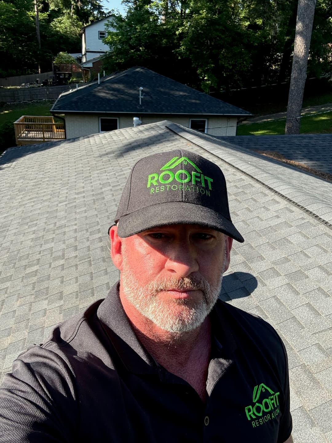 Man on a rooftop wearing a RooFit Restoration cap, showcasing shingles and surroundings.