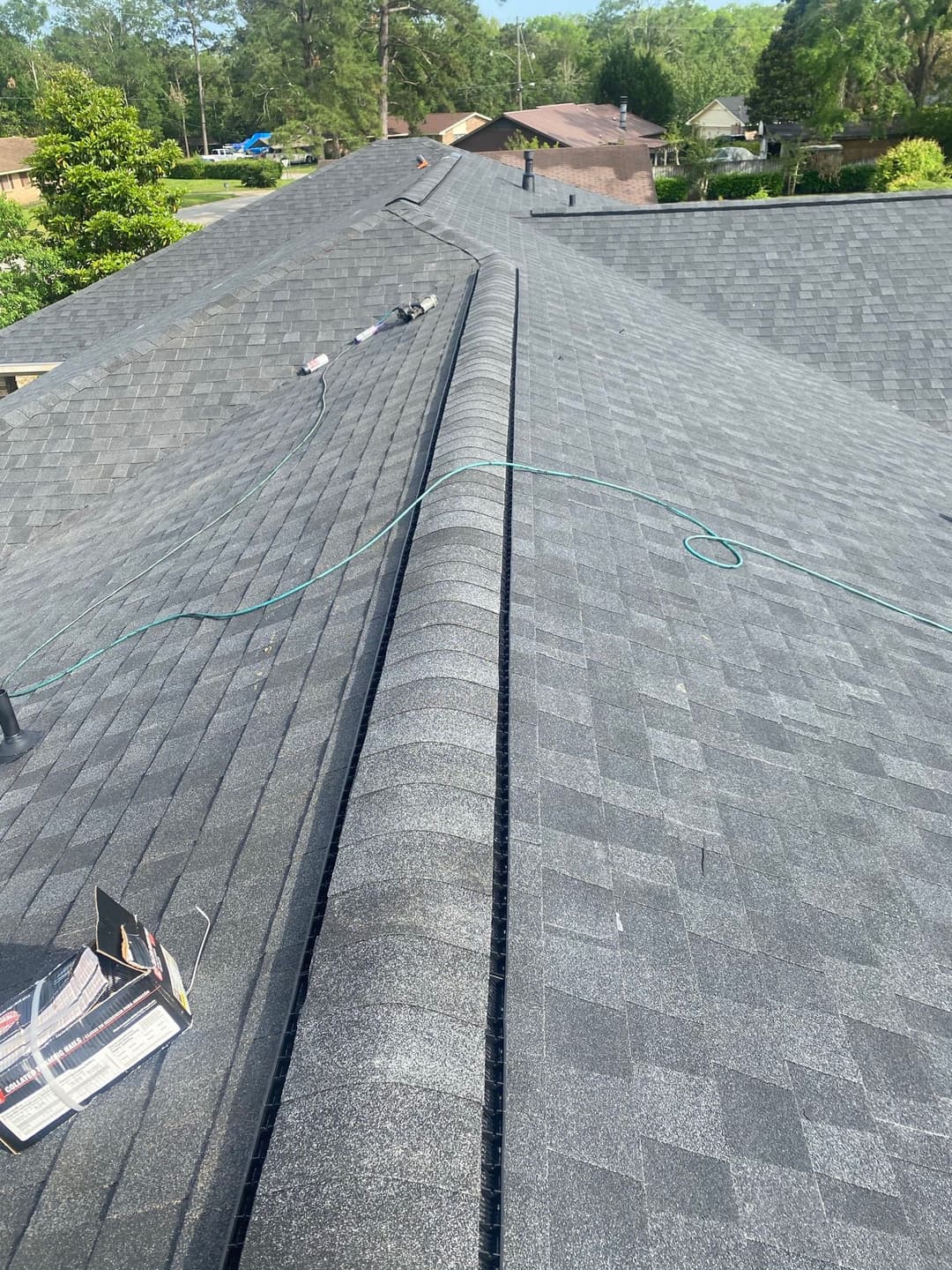 Roofing installation process on a gray shingle roof, showing seamless shingles and tools.