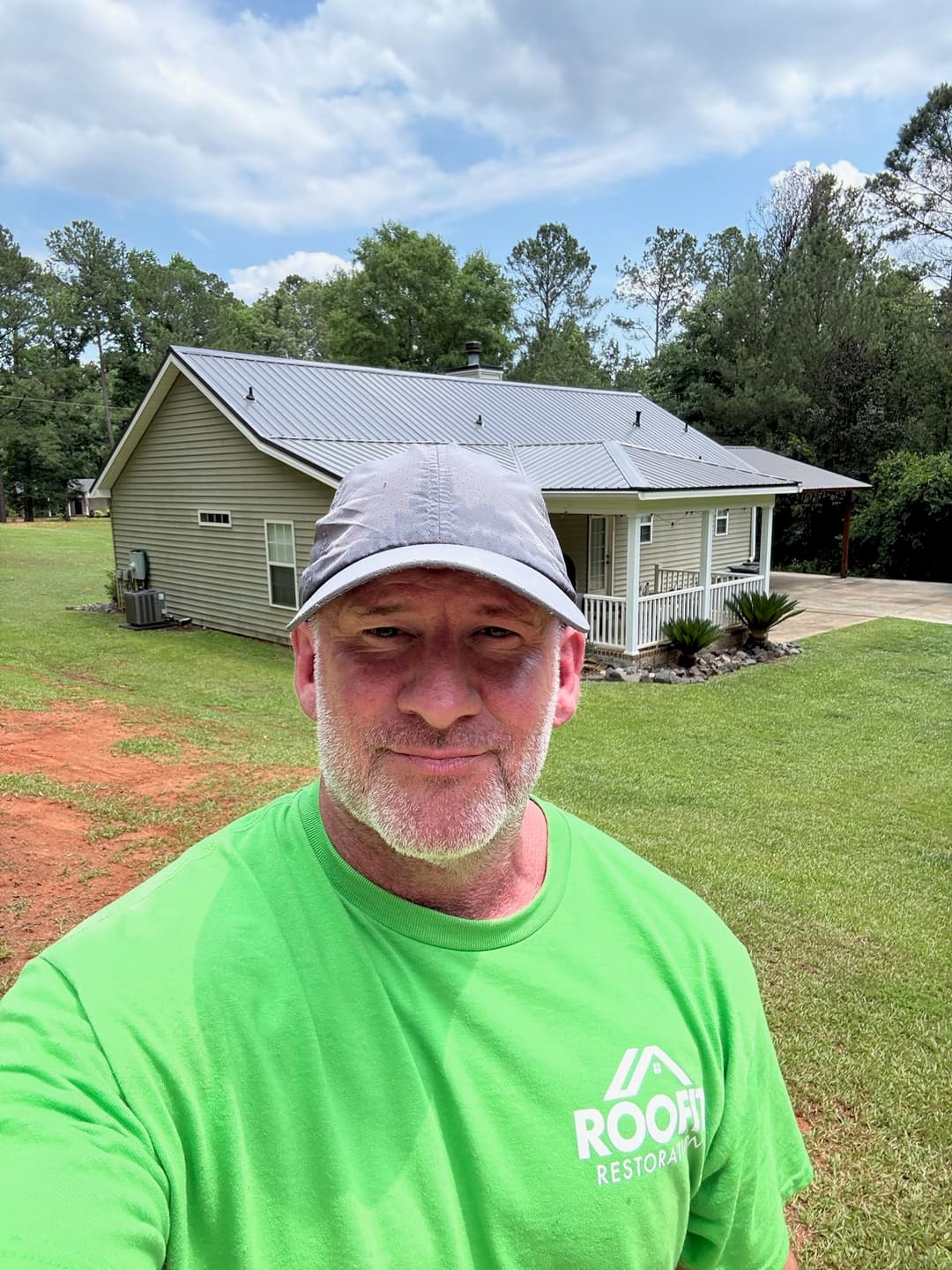 Man in green shirt stands in front of a house with a new roof and grassy yard.
