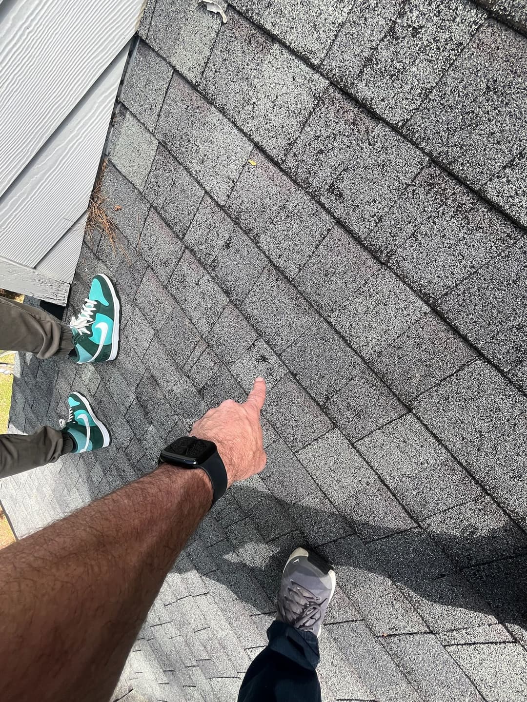 Person pointing at roofing shingles while wearing distinct sneakers on a sloped roof.