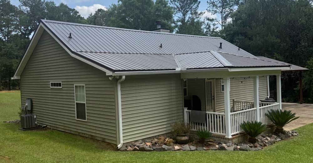 Metal-roofed home with porch in a lush green yard surrounded by trees.