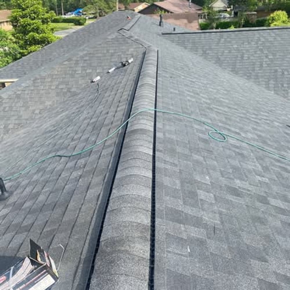 A close-up view of a gray shingle roof with a hose on a sunny day.